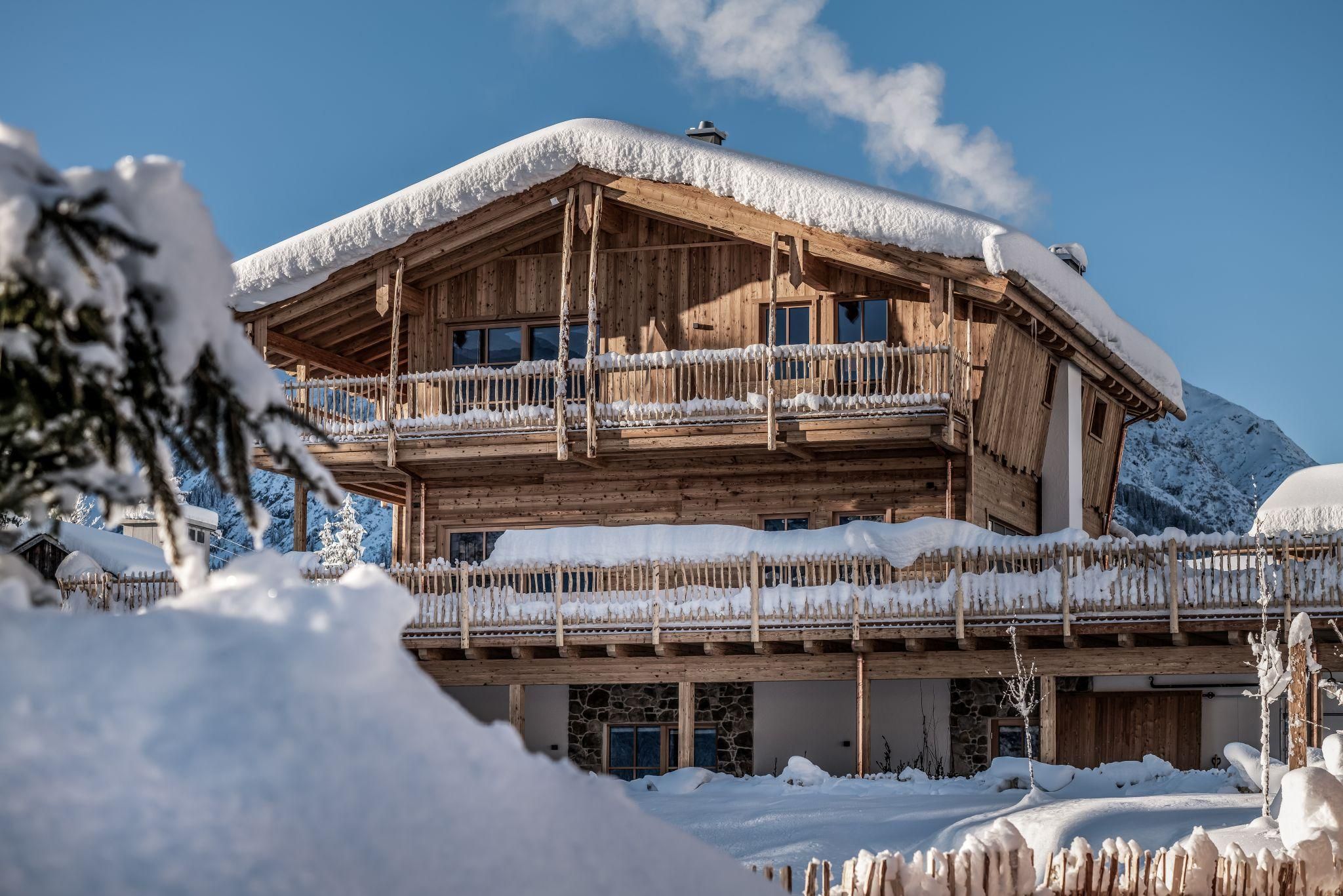 A beautiful chalet in winter with a snow-covered roof and wooden cladding. The surroundings are characterized by white snow and a blue sky.