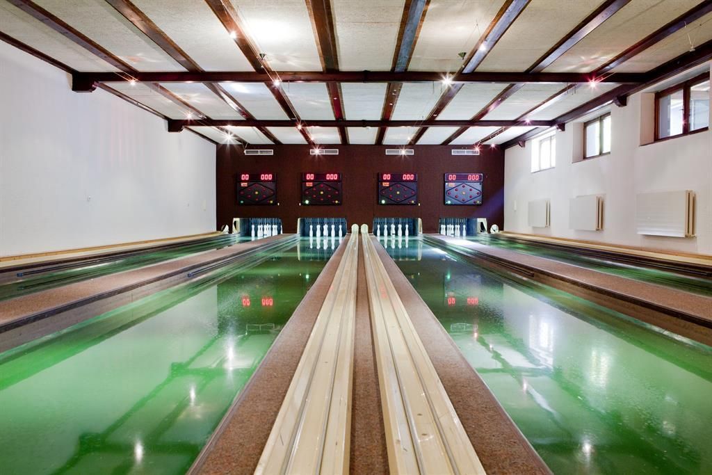 A bowling area with several bowling lanes and colorful lighting. The walls are simple, and the atmosphere feels inviting.