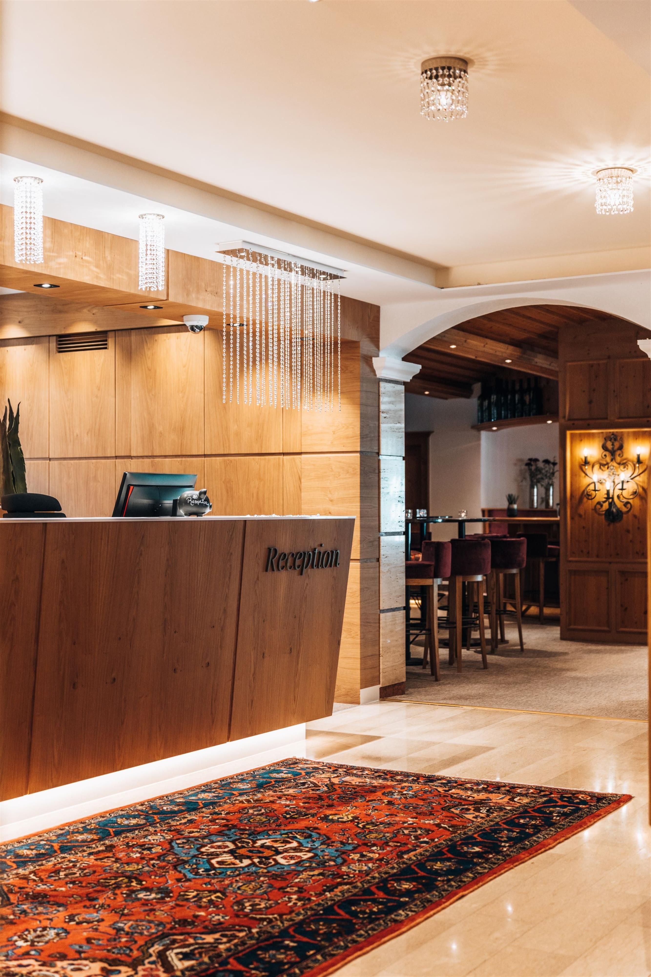 An elegant reception area with wooden paneling and a beautiful carpet. In the background, seating and a bar are visible.