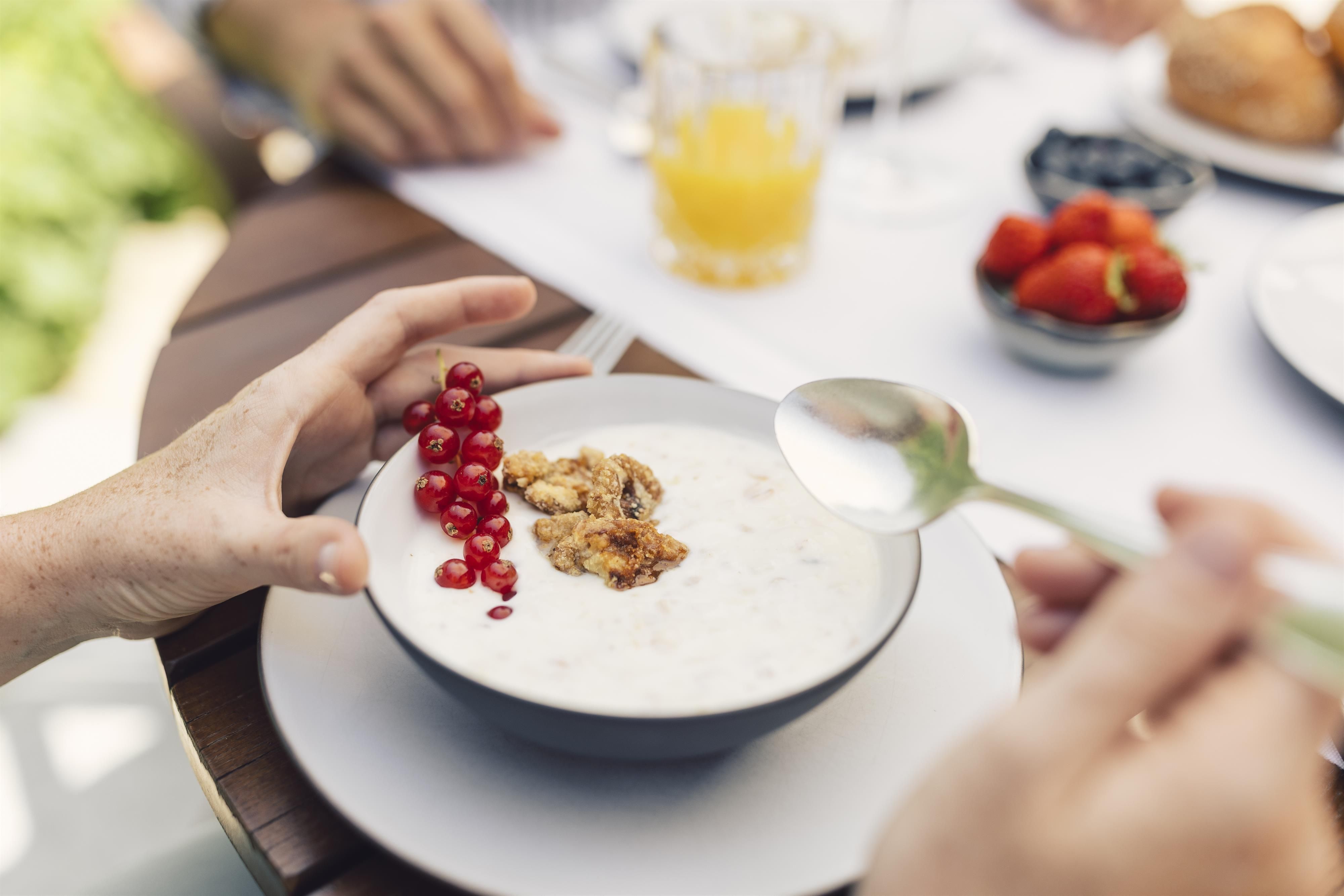 A healthy breakfast with yogurt, fresh red currants, and oatmeal. In the background, more breakfast dishes and drinks can be seen.