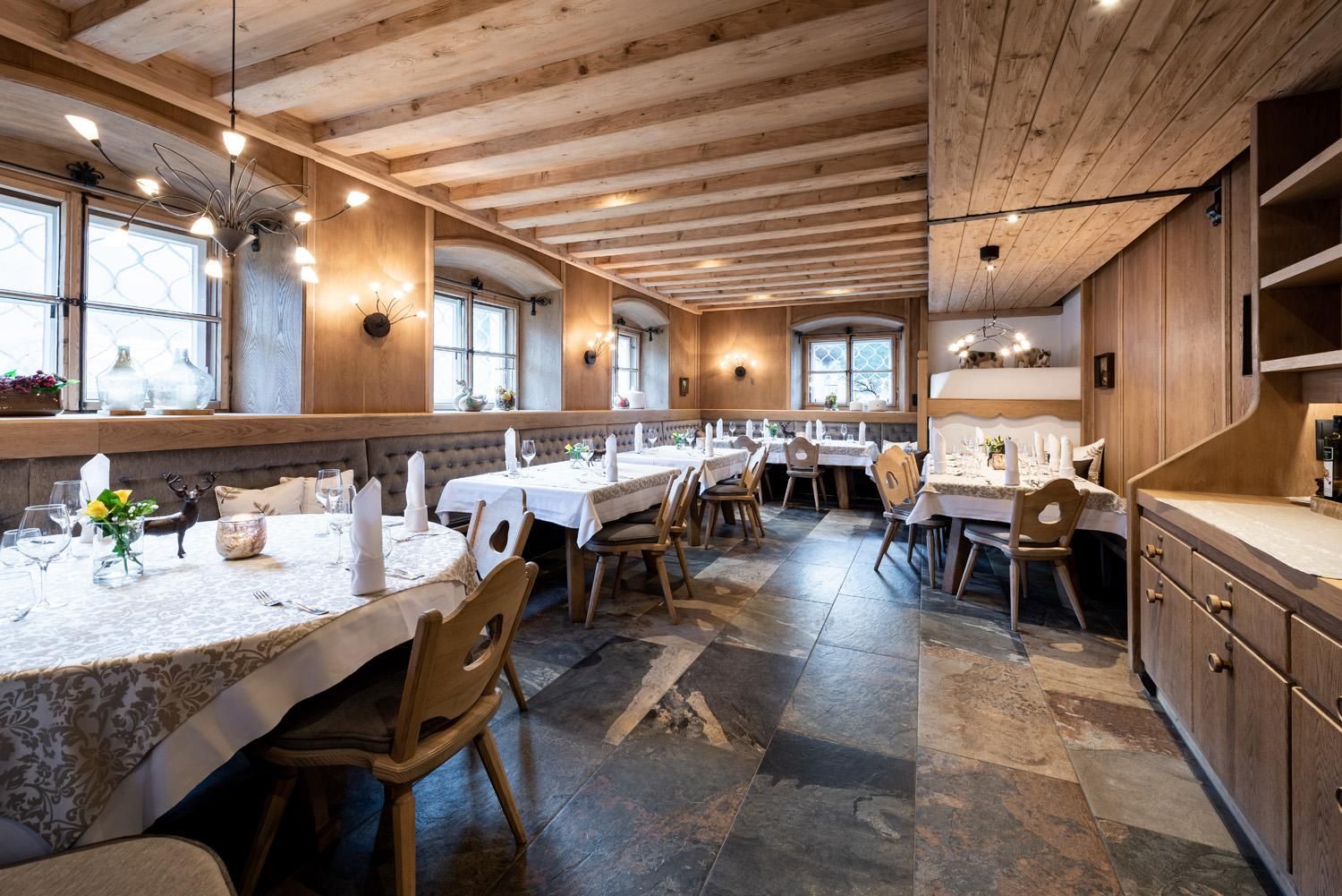 A cozy restaurant with wooden decor and warm lighting. The tables are lovingly set and invite you to dine.