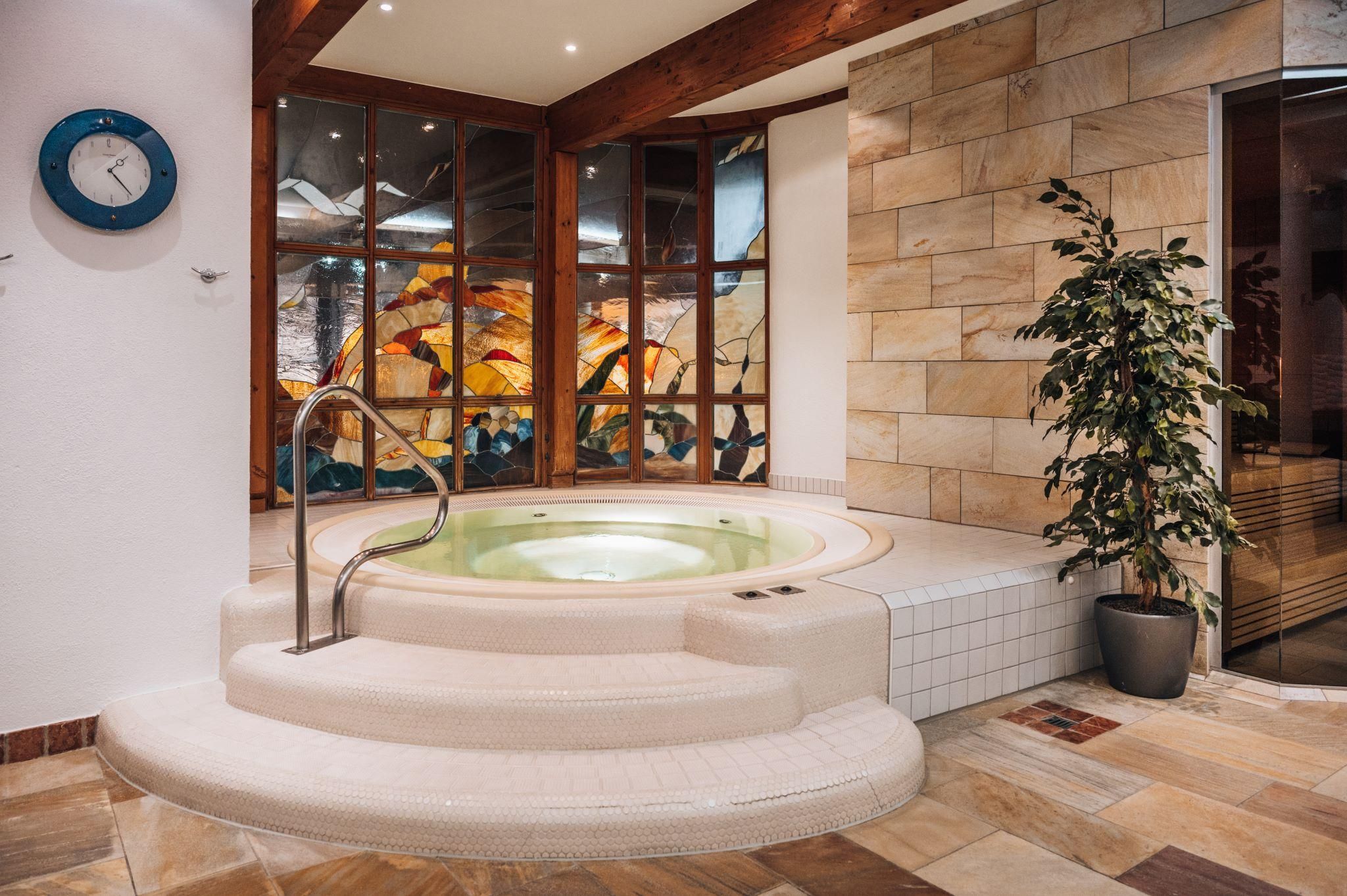 A modern wellness area with a hot tub and large windows that let in plenty of light. Relaxed atmosphere with a plant in the corner.