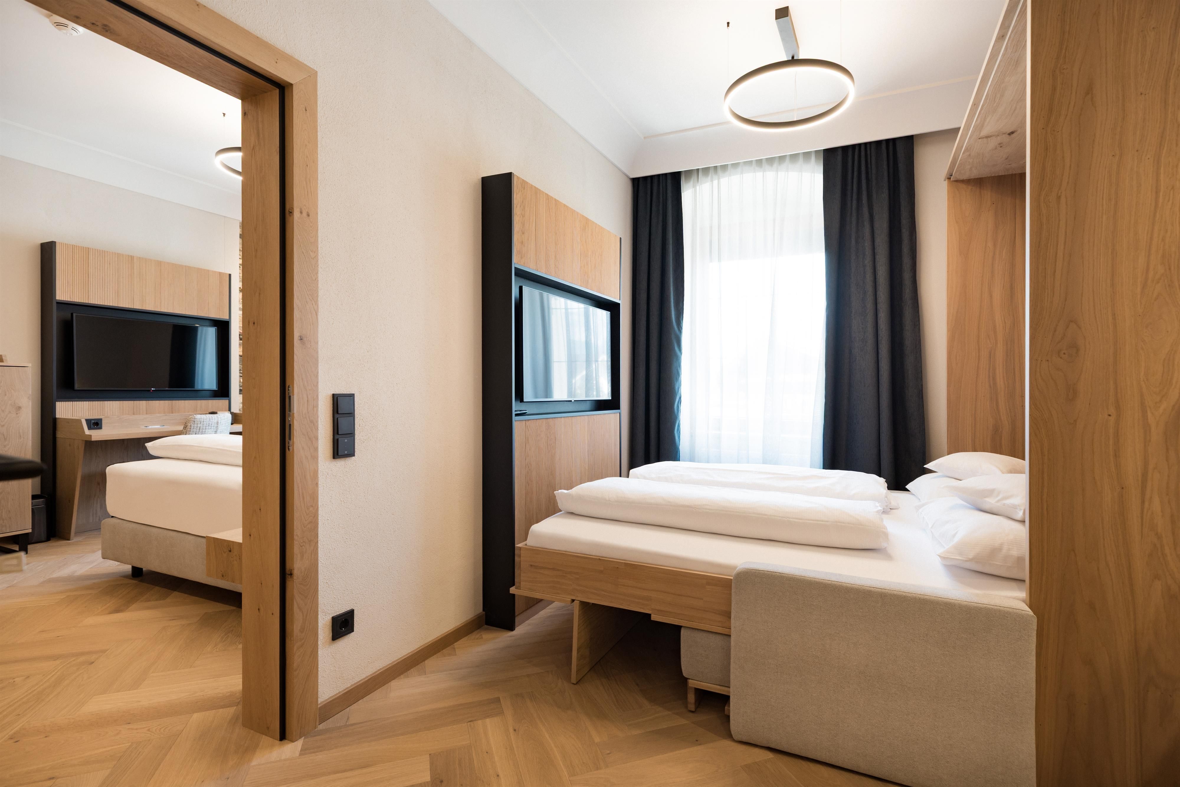 A modern room with two beds and a television. Large windows provide plenty of natural light.