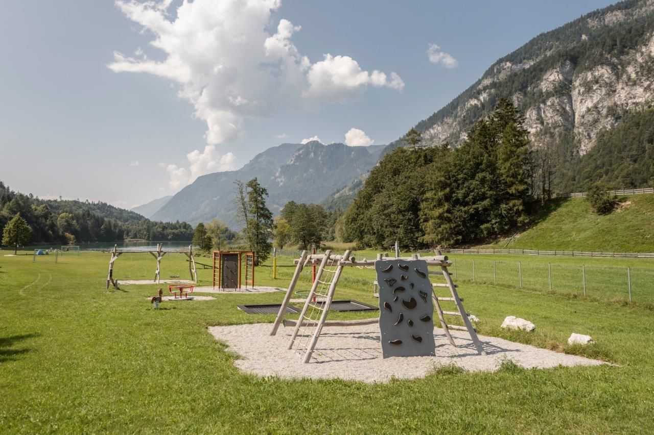 A playground in a green meadow with mountains in the background. There are climbing frames and a climbing rock for playing.
