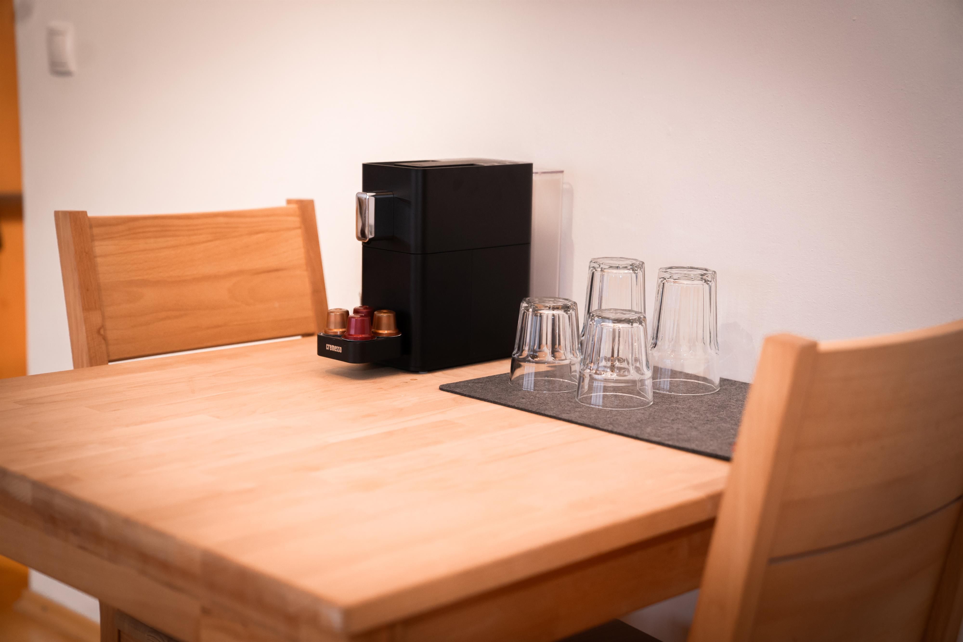 A wooden table with two chairs and a coffee machine. On the table are some glasses and a coaster.
