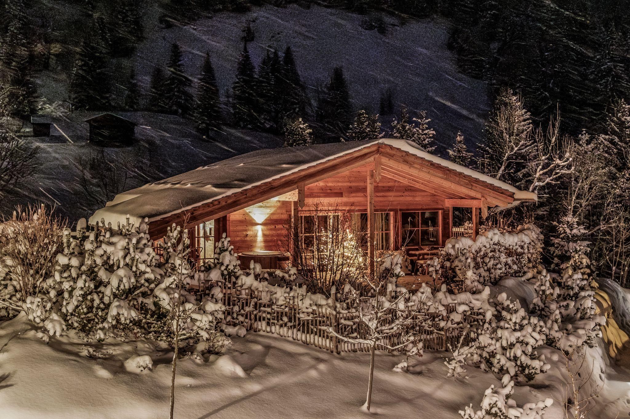 A cozy chalet in a snowy landscape at night. Soft lights shine through the windows and create a warm atmosphere.