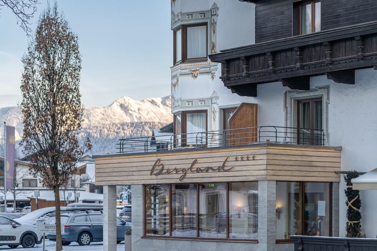 A charming hotel with a modern facade and wood cladding. Snow-capped mountains are visible in the background.