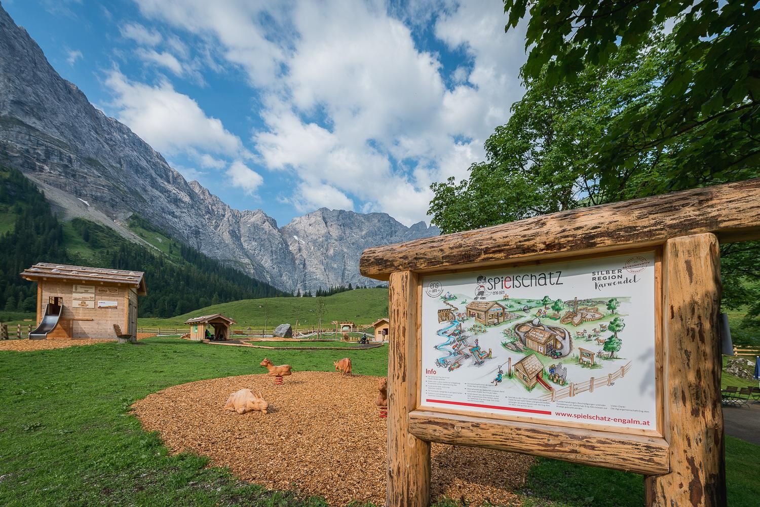 A picturesque farmhouse in a mountain landscape. In the foreground, there is an information sign with a map of the area.