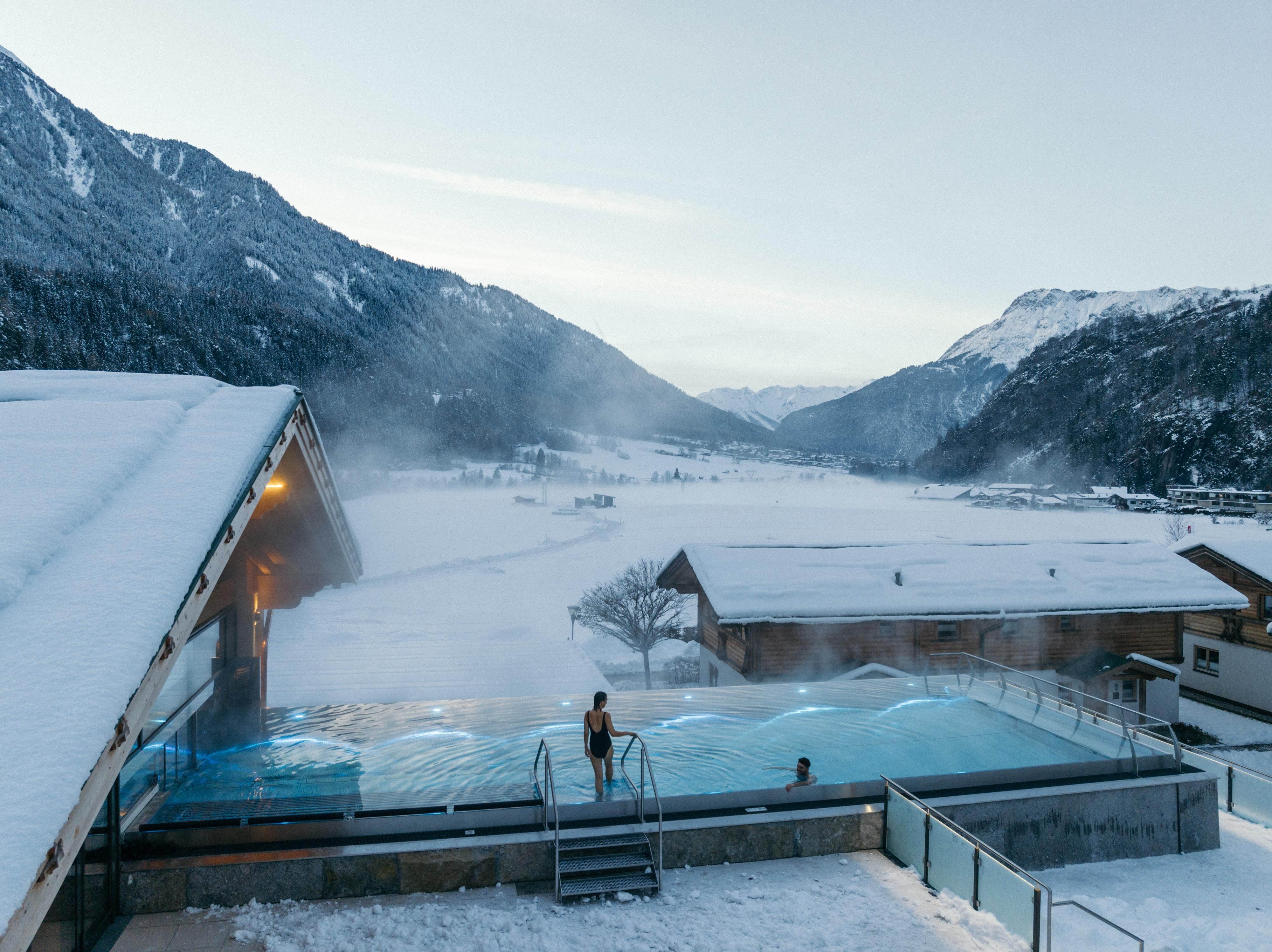 A luxurious outdoor pool in the mountains, surrounded by snow-covered landscapes. The steaming water surface creates a relaxing atmosphere.