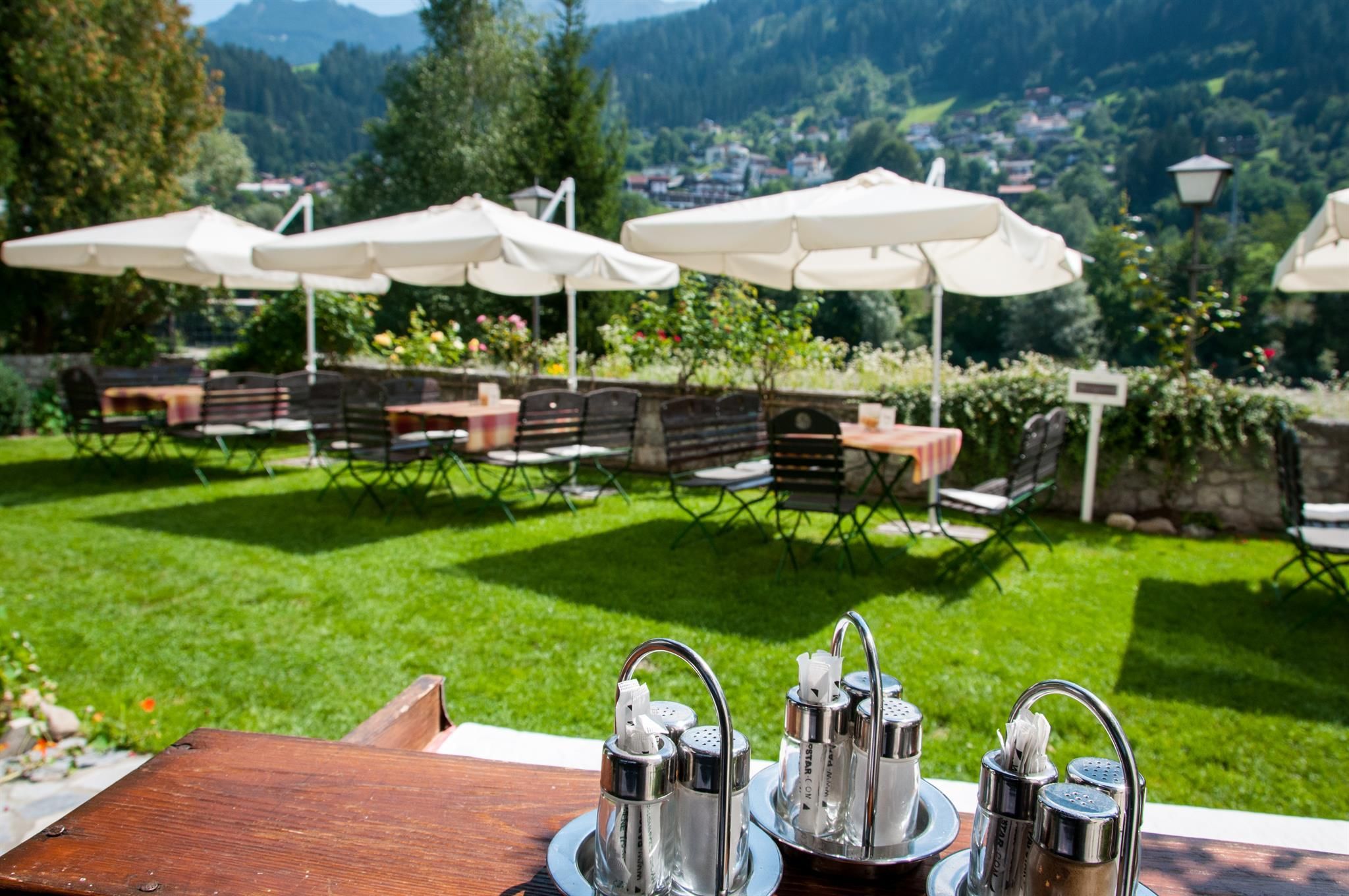 A beautiful garden with green grass and sun umbrellas. In the foreground, there are teapots on a tray.